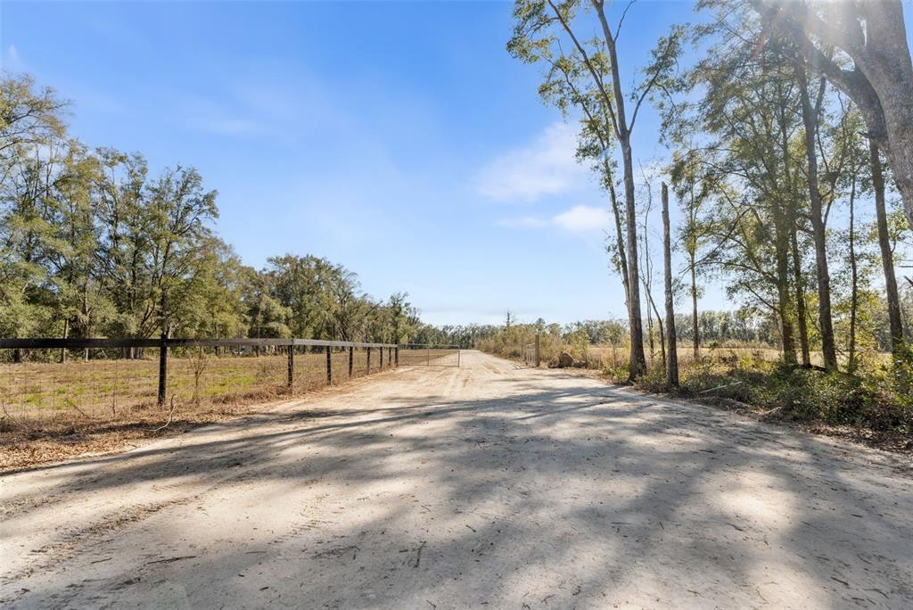 A dirt road leads toward a metal gate between a fenced pasture and trees — 17807 SW 83RD AVENUE, ARCHER, FL