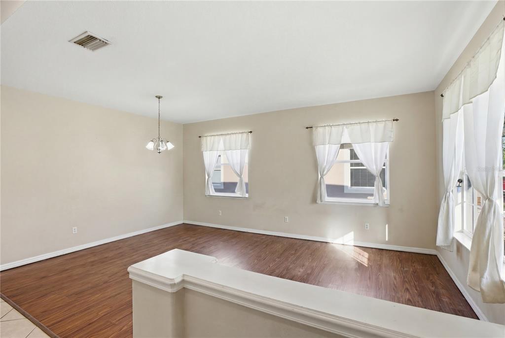 An empty dining room features wood-look flooring, beige walls, and two windows with white curtains — 12512 23RD STREET E, PARRISH, FL