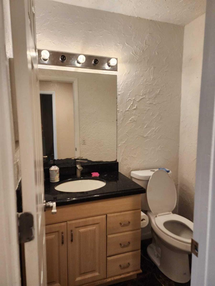A small bathroom features a light wood vanity, black countertop, and a wall-mounted light fixture — 2790 NW 80th Avenue, Sunrise FL 33322, SUNRISE, FL
