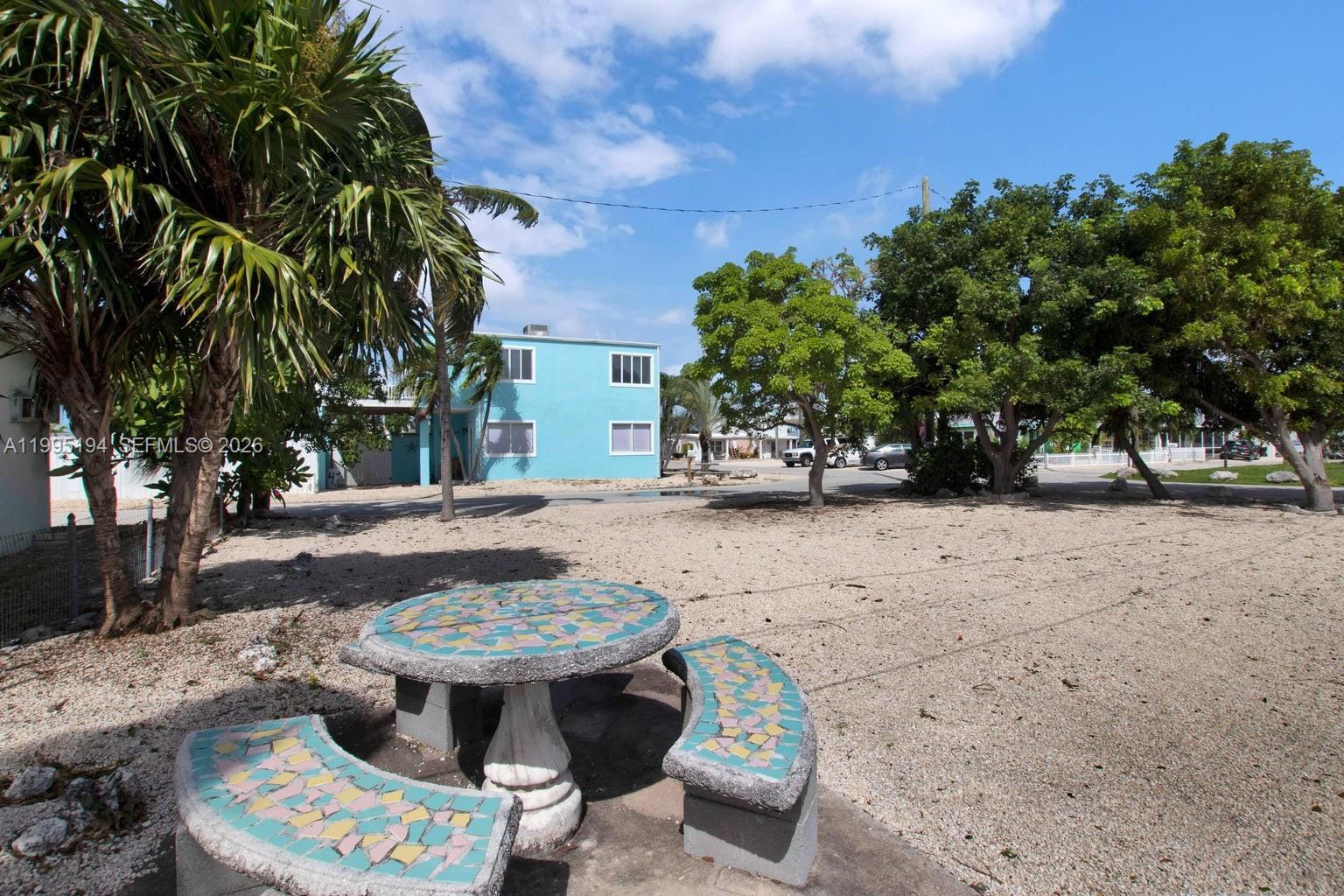 A mosaic-tiled stone table and curved benches sit in a gravel yard near a blue building — Lot 70 5th Ave Ocean, Marathon FL 33050, MARATHON, FL