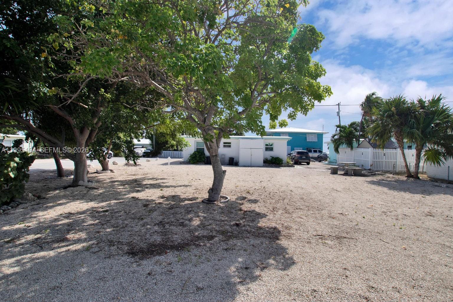 A gravel yard with several trees sits in front of a small, light-colored building — Lot 70 5th Ave Ocean, Marathon FL 33050, MARATHON, FL