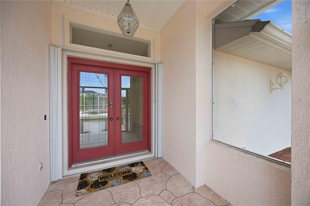 A covered entryway features a red double door, a patterned welcome mat, and stone flooring — 63 CLUBHOUSE ROAD, ROTONDA WEST, FL