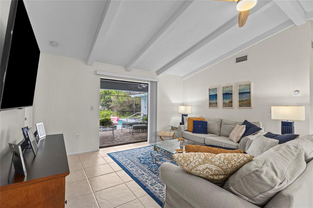A living room features vaulted ceilings, tile floors, a blue area rug, and patio access — 4308 PASADENA CIRCLE, SARASOTA, FL