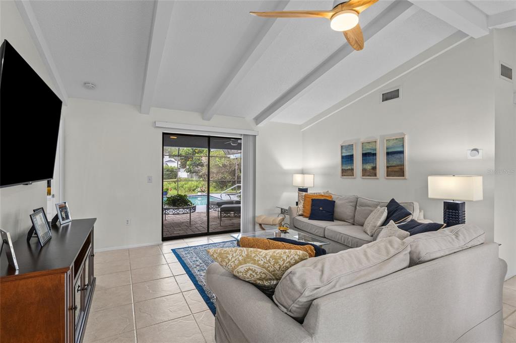A living room with vaulted ceilings, tile floors, and a sliding door leading to a pool — 4308 PASADENA CIRCLE, SARASOTA, FL