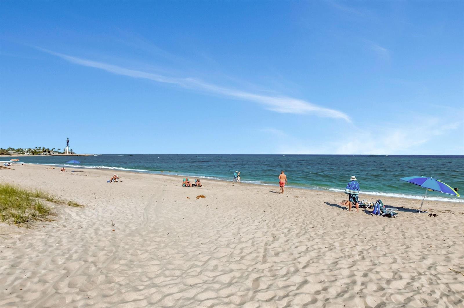 A sandy beach with people, beach umbrellas, and a distant lighthouse under a clear sky — 1776 Bay Drive, Pompano Beach FL 33062, POMPANO BEACH, FL