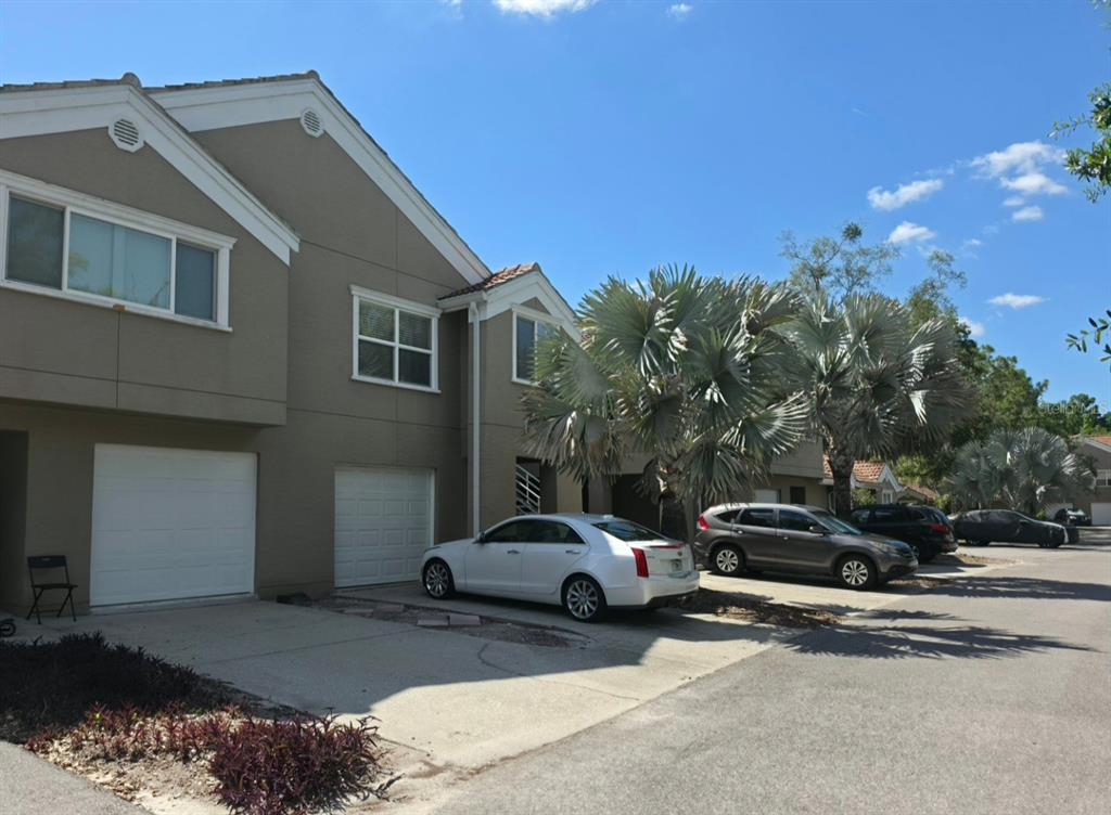 A two-story townhouse exterior with a white garage door, a white sedan, and palm trees — 15215 AMBERLY DRIVE UNIT 907, TAMPA, FL