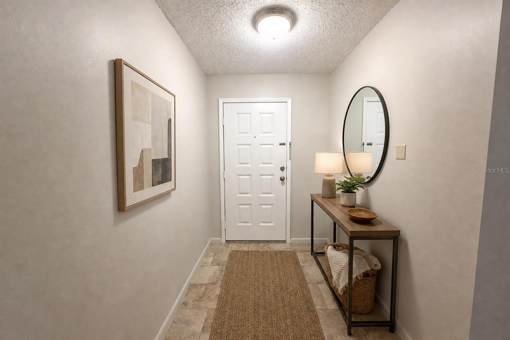 An entryway features a white door, a console table with a mirror, and tile flooring — 15215 AMBERLY DRIVE UNIT 907, TAMPA, FL