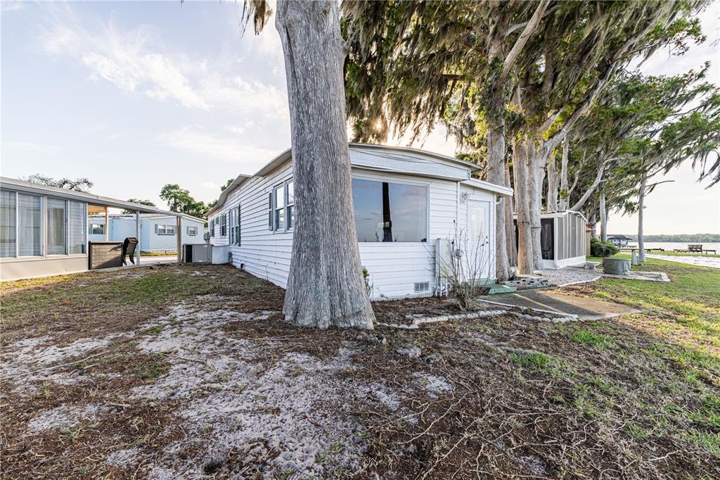 A white mobile home sits on a sandy lot near trees and a lake — 12315 US HIGHWAY 441 UNIT 23, TAVARES, FL