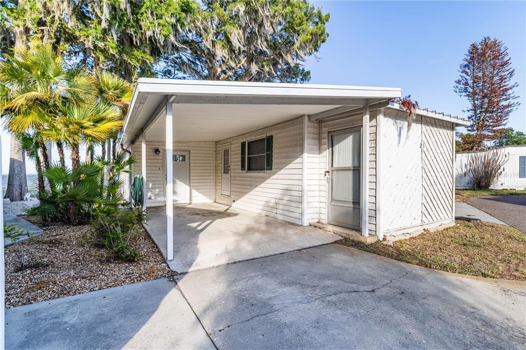 A white mobile home features a concrete carport, a screen door, and surrounding palm trees — 12315 US HIGHWAY 441 UNIT 23, TAVARES, FL
