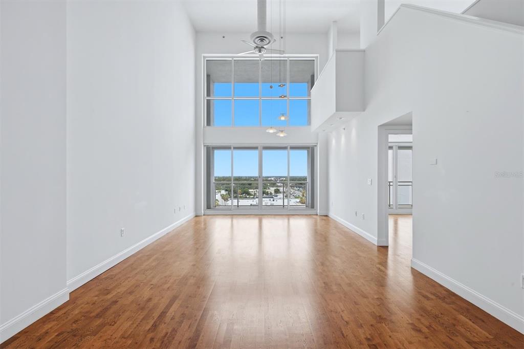 A bright, empty living room features high ceilings, hardwood floors, and large floor-to-ceiling windows — 1990 MAIN STREET UNIT 4, SARASOTA, FL