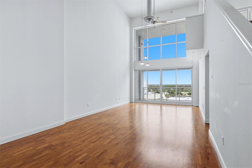 A bright, empty living room features high ceilings, hardwood floors, and large floor-to-ceiling windows — 1990 MAIN STREET UNIT 4, SARASOTA, FL