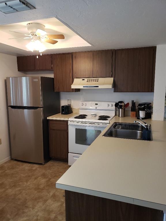A kitchen features dark wood cabinets, stainless steel appliances, a white stove, and a peninsula counter — 25225 RAMPART BOULEVARD UNIT 1908, PUNTA GORDA, FL
