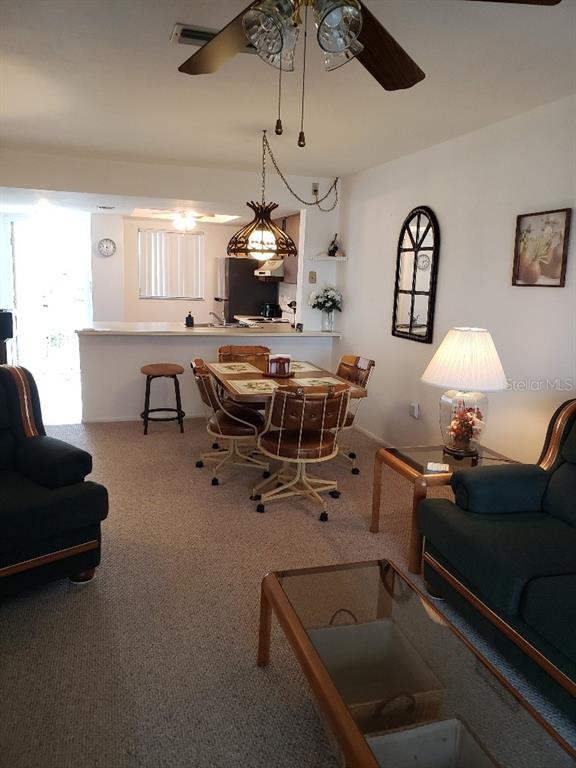 A living room and dining area feature carpeted floors, a ceiling fan, and a breakfast bar — 25225 RAMPART BOULEVARD UNIT 1908, PUNTA GORDA, FL