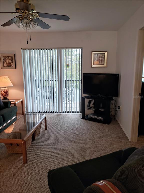 A living room features a ceiling fan, a television on a stand, and sliding glass doors — 25225 RAMPART BOULEVARD UNIT 1908, PUNTA GORDA, FL