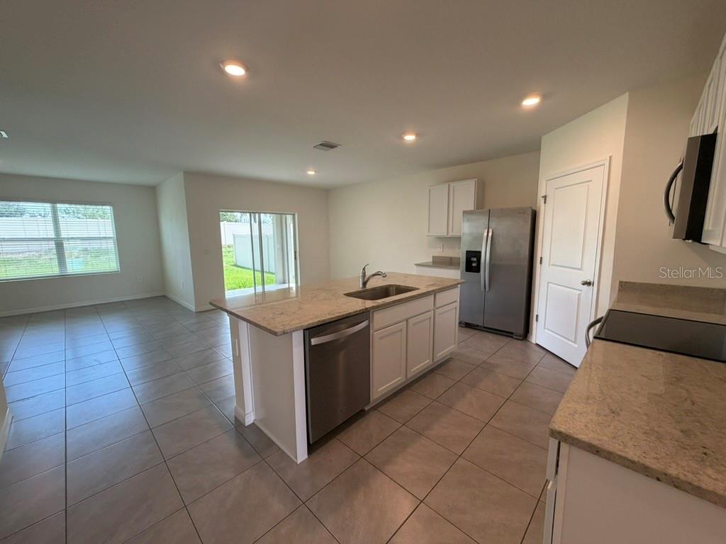 A kitchen with white cabinets, granite countertops, and stainless steel appliances opens to a living area — 17819 CANOPY PLACE, BRADENTON, FL