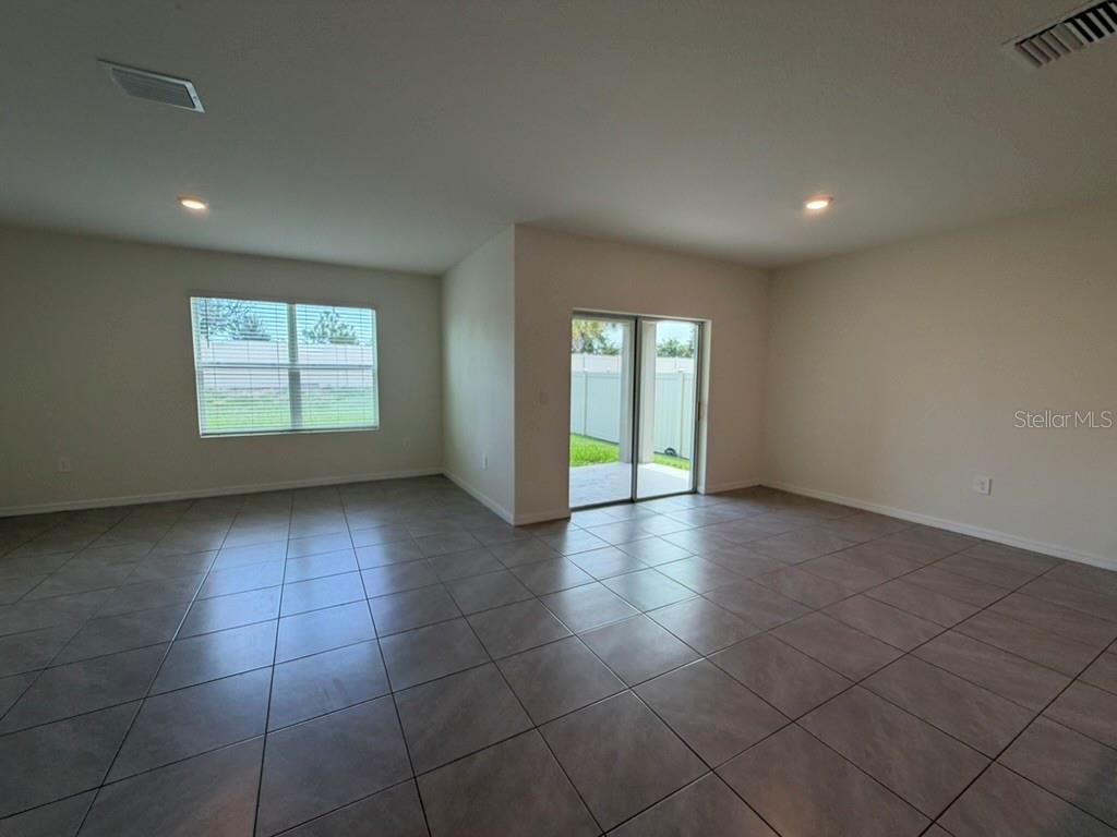 An empty room with large floor tiles, a window, and sliding glass doors to a patio — 17819 CANOPY PLACE, BRADENTON, FL