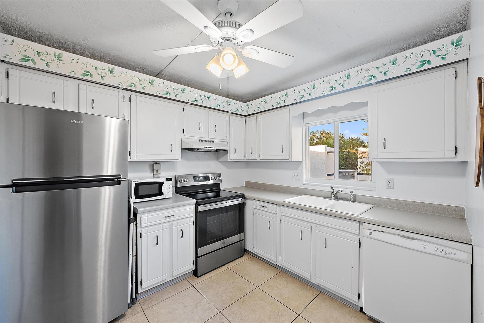 A bright, open-concept living and dining area features tile flooring, neutral furniture, and modern decor — 1561 NE 12th Terrace # 14, Jensen Beach FL 34957, JENSEN BEACH, FL