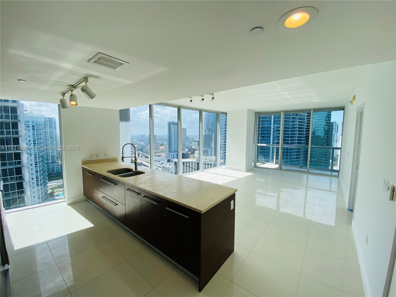 A modern kitchen with dark wood cabinets and light countertops overlooks a city skyline — 475 Brickell Ave # 3715, Miami FL 33131, MIAMI, FL