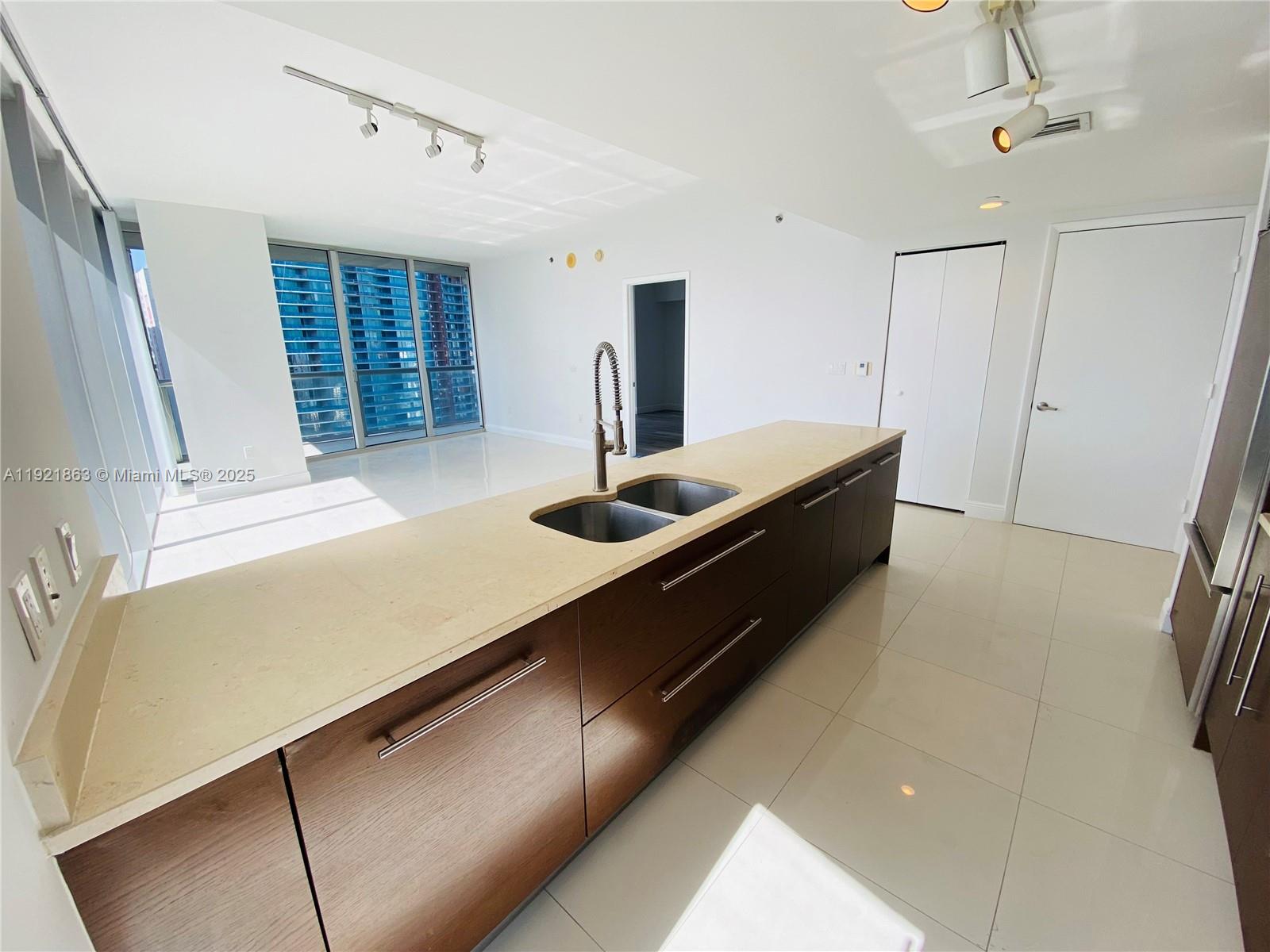 A modern kitchen features dark wood cabinetry, a light stone countertop, and tile flooring — 475 Brickell Ave # 3715, Miami FL 33131, MIAMI, FL