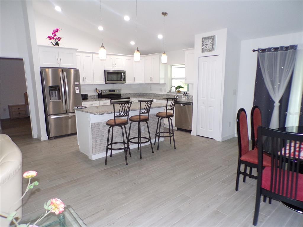 A kitchen with white cabinets, stainless steel appliances, a granite island, and wood-look tile flooring — 334 MILLPORT STREET NW, PORT CHARLOTTE, FL