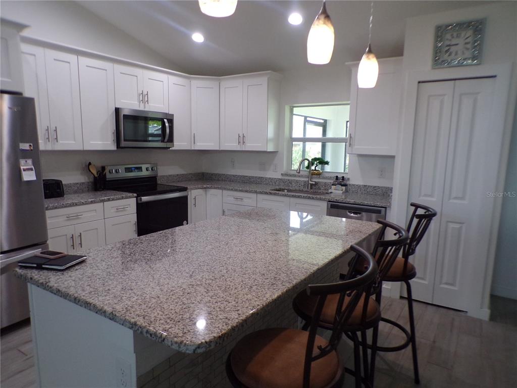 A kitchen features white cabinets, granite countertops, a central island, and two bar stools — 334 MILLPORT STREET NW, PORT CHARLOTTE, FL