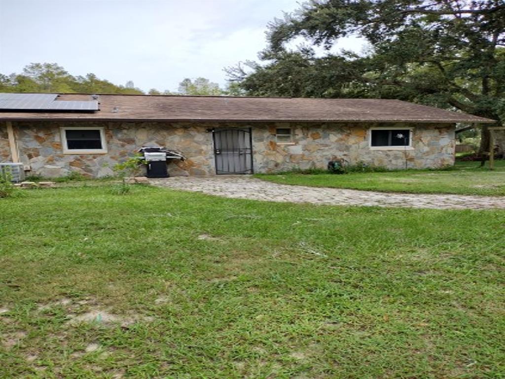A stone-clad house exterior features a brown shingled roof and a paved walkway — 18334 SPENCER ROAD, ODESSA, FL