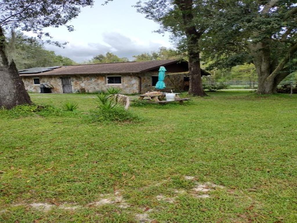 A stone-faced house sits on a grassy lot surrounded by large trees — 18334 SPENCER ROAD, ODESSA, FL