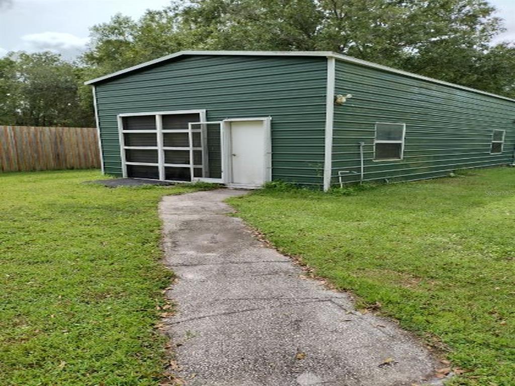 A green metal-sided building with a white door and a concrete walkway in a yard — 18334 SPENCER ROAD, ODESSA, FL