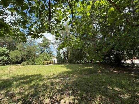 A grassy, partially shaded lot with mature trees and foliage in the background — 00 SE 71ST AVENUE, HAWTHORNE, FL