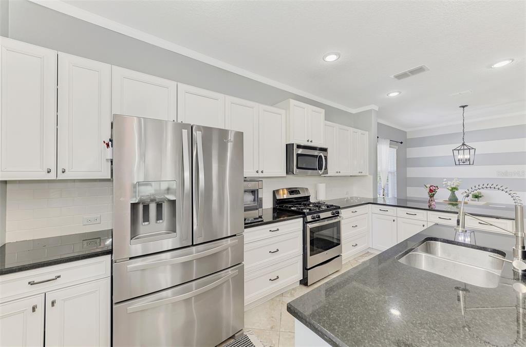 A modern kitchen features white cabinets, stainless steel appliances, and a dark granite island countertop — 5008 MISSION PARK LANE, BRADENTON, FL