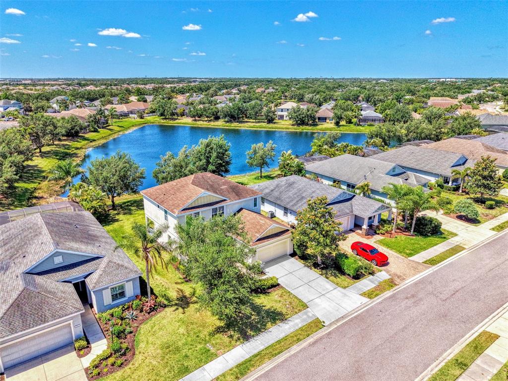 An aerial view shows suburban houses with driveways and lawns bordering a large pond — 5008 MISSION PARK LANE, BRADENTON, FL
