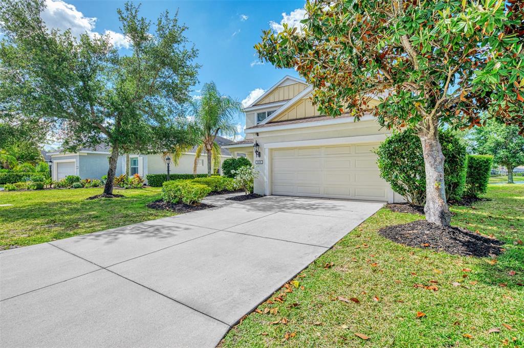 A concrete driveway leads to the two-car garage of a suburban house with landscaping — 5008 MISSION PARK LANE, BRADENTON, FL