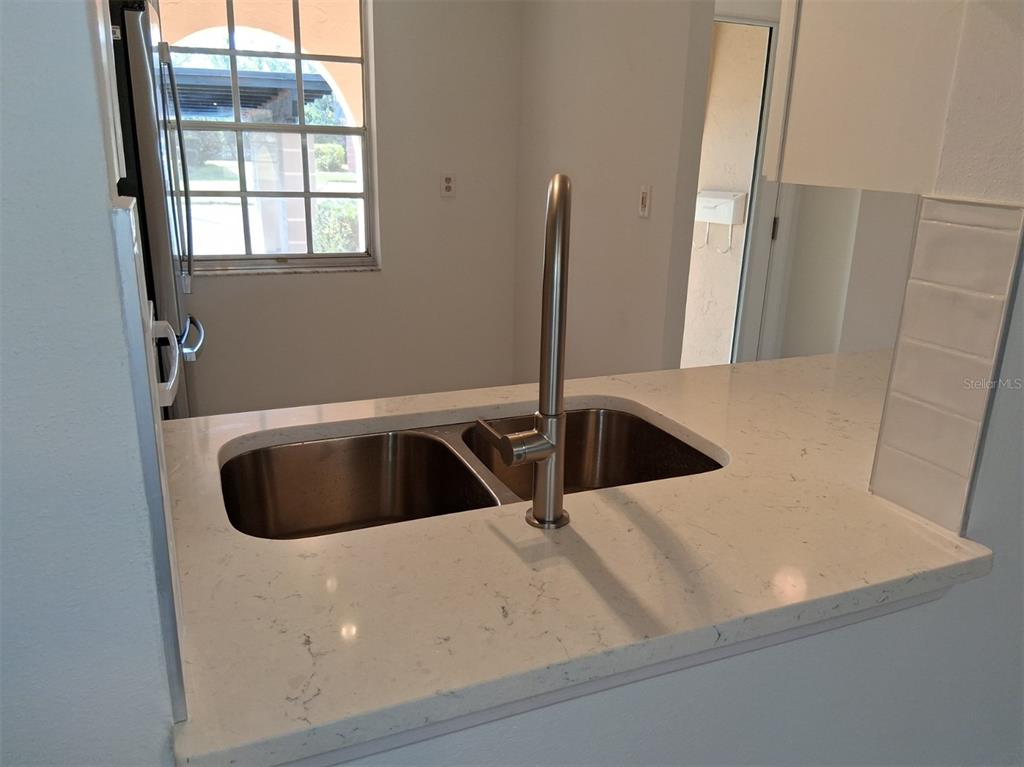 A kitchen features a double-basin stainless steel sink with a tall faucet on a white countertop — 4326 SUMMERSUN DRIVE, NEW PORT RICHEY, FL