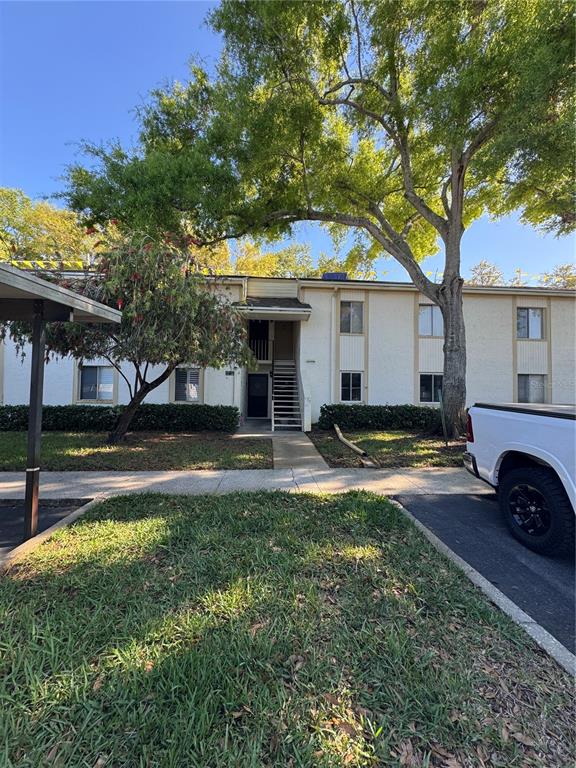 A two-story apartment building exterior features a central staircase, a parking area, and mature trees — 109 PINE COURT, OLDSMAR, FL