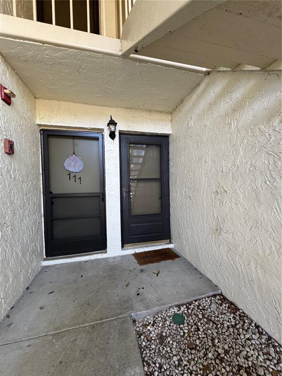 An exterior view of a building entrance featuring two dark screen doors and stucco walls — 109 PINE COURT, OLDSMAR, FL
