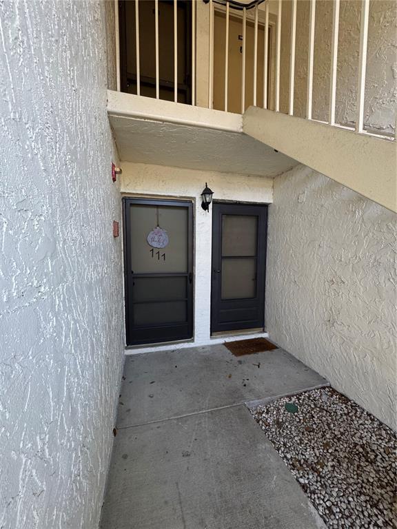 An exterior view of two ground-level apartment doors with a staircase leading to an upper level — 109 PINE COURT, OLDSMAR, FL