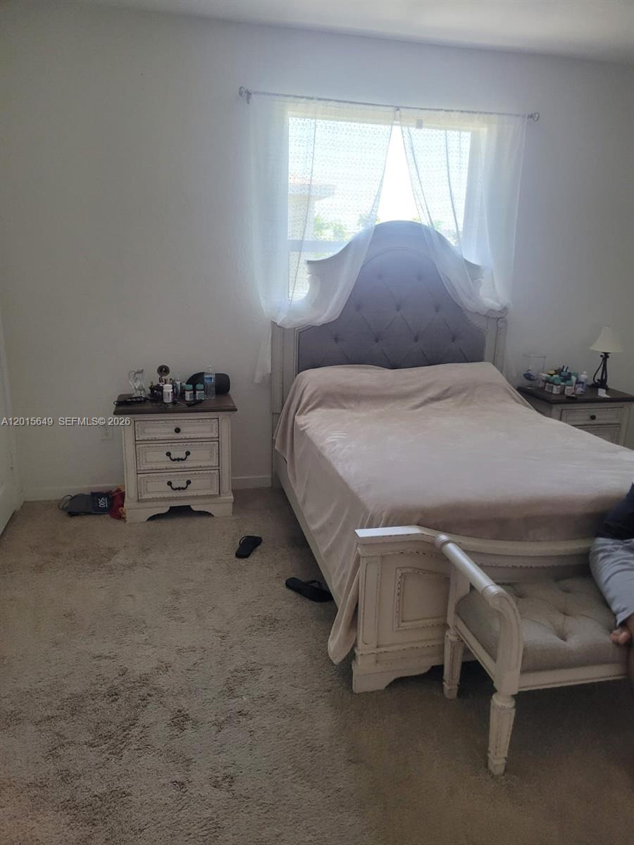 A bedroom features a tufted headboard bed, two nightstands, and a bench on carpeted flooring — 441 NE 5th St, Florida City FL 33034, FLORIDA CITY, FL