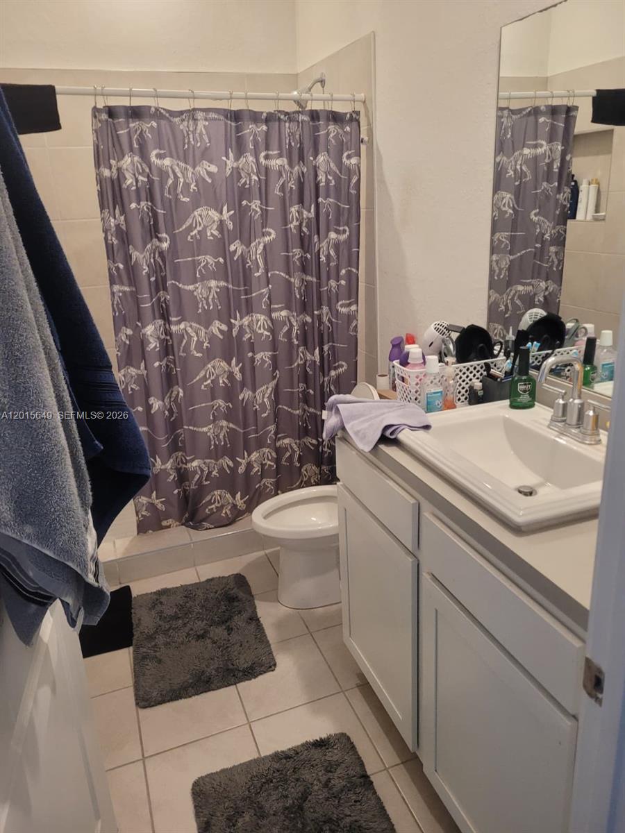 A bathroom features a dinosaur-patterned shower curtain, a white vanity, and light-colored floor tiles — 441 NE 5th St, Florida City FL 33034, FLORIDA CITY, FL