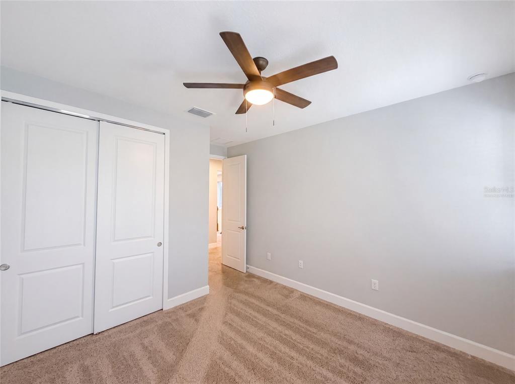 A bedroom with light gray walls, beige carpet, a ceiling fan, and white closet doors — 13720 STEVENSON LANE, ODESSA, FL