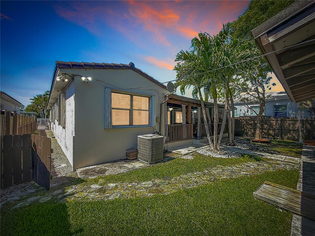 The backyard features a house exterior, a stone pathway, palm trees, and a wooden fence — 821 83RD ST, MIAMI BEACH, FL