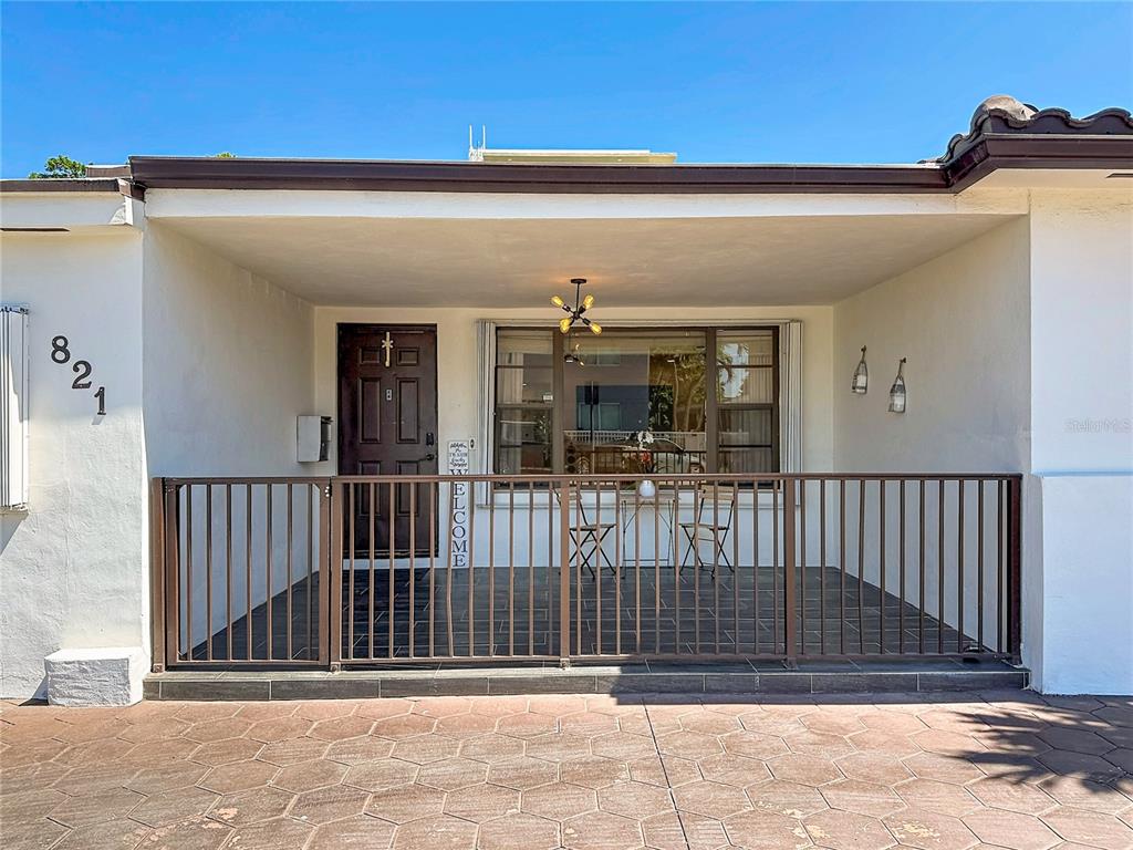 A covered front porch features a metal railing, tiled flooring, and a dark entry door — 821 83RD ST, MIAMI BEACH, FL