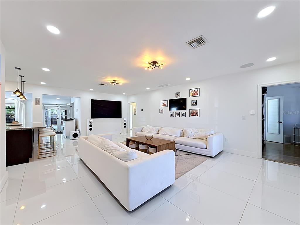 A bright, open-concept living room features white tile floors, white sofas, and a large television — 821 83RD ST, MIAMI BEACH, FL