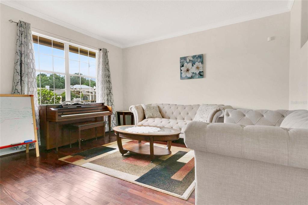 A living room features a piano, a tufted sofa, a coffee table, and hardwood floors — 8044 CANYON LAKE CIRCLE, ORLANDO, FL