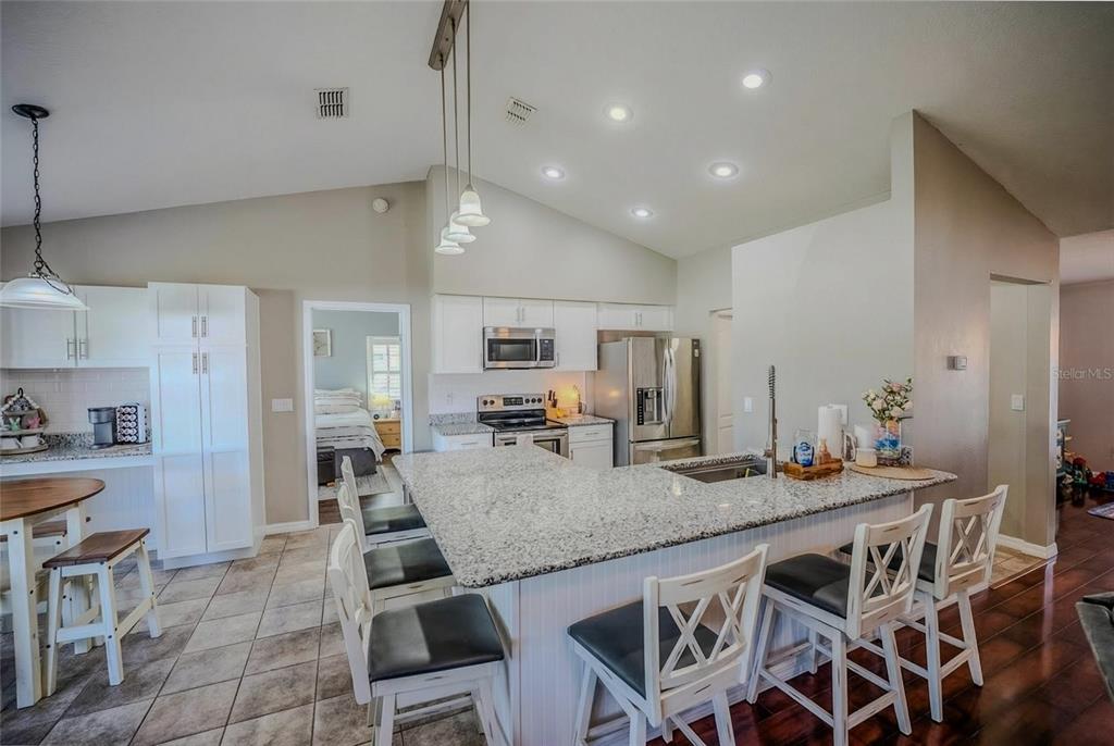 A kitchen features white cabinetry, granite countertops, a large island with seating, and tile flooring — 4719 SE 32ND STREET, OCALA, FL