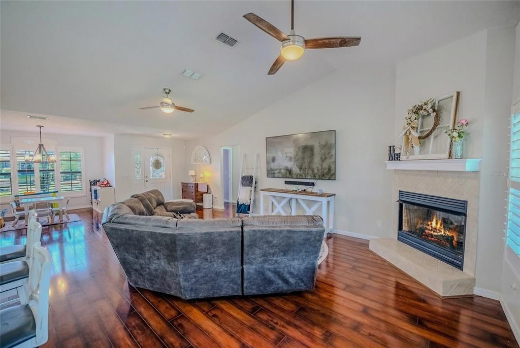 A living room with a gray sectional sofa, fireplace, and hardwood floors under vaulted ceilings — 4719 SE 32ND STREET, OCALA, FL