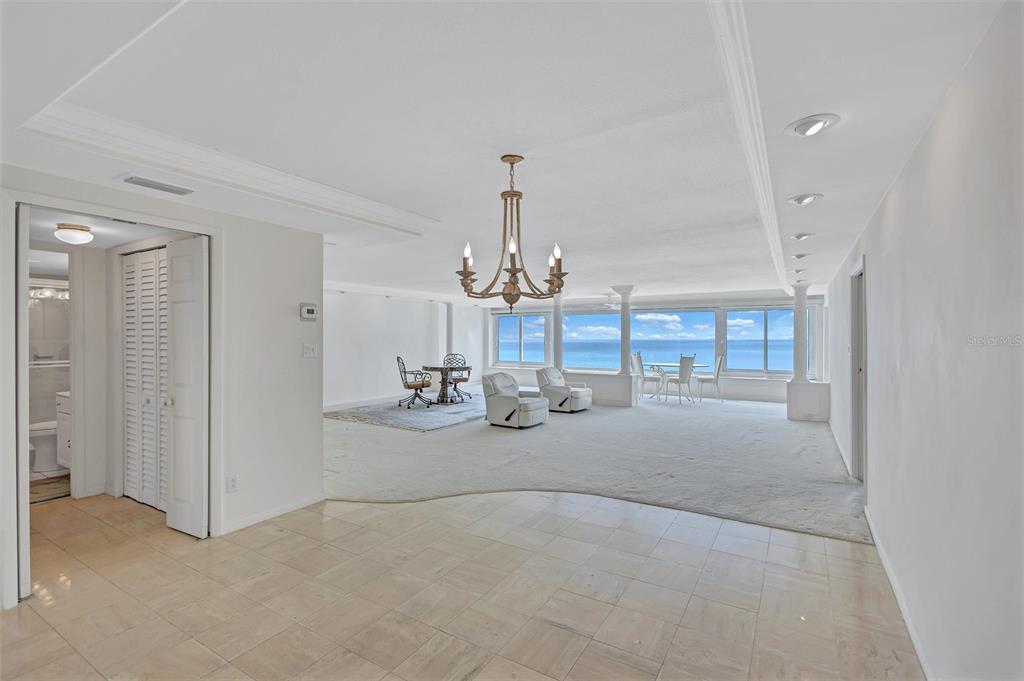 A spacious living area with white carpeting, a chandelier, and floor-to-ceiling ocean views — 6140 MIDNIGHT PASS ROAD UNIT 904, SARASOTA, FL
