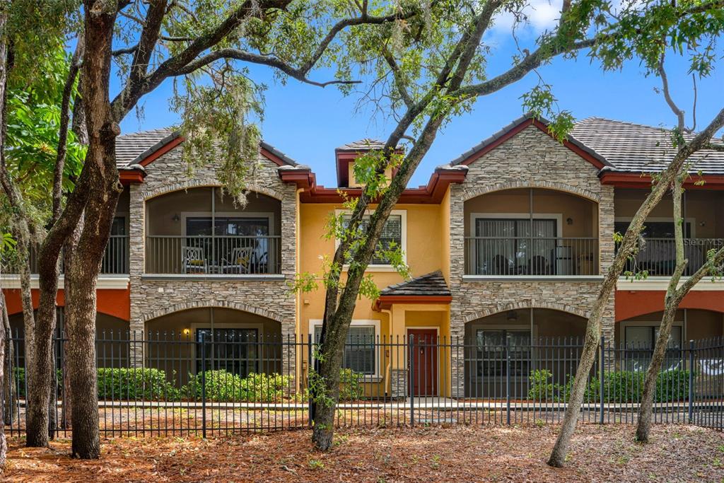 A two-story apartment building with stone accents, screened balconies, and a black metal fence — 2250 PORTOFINO PLACE UNIT 239, PALM HARBOR, FL