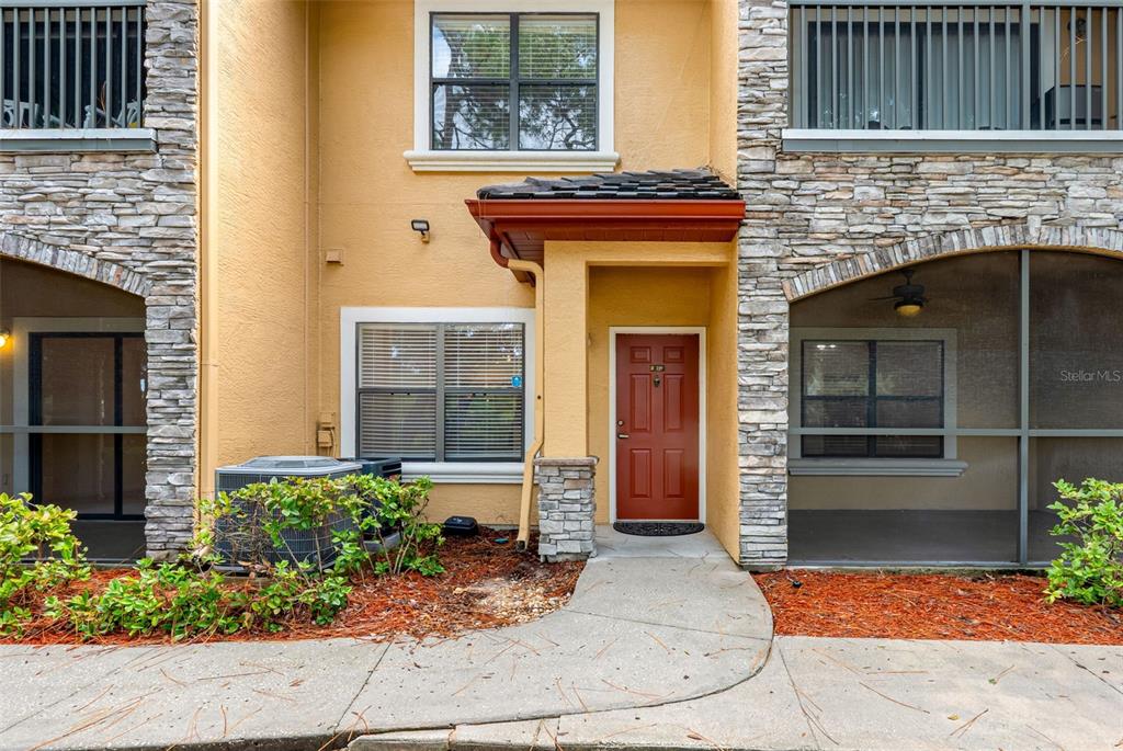 A tan stucco townhouse exterior features a red front door, stone accents, and screened porches — 2250 PORTOFINO PLACE UNIT 239, PALM HARBOR, FL