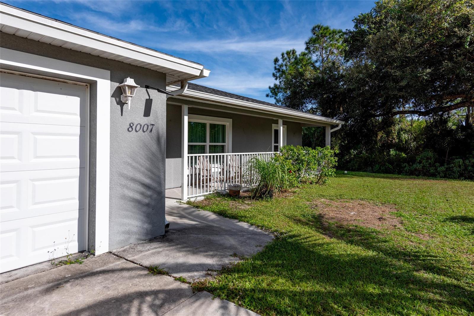 A gray house exterior features a white garage door, a front porch, and a lawn — 8007 Royal Court, FL 33935, FL