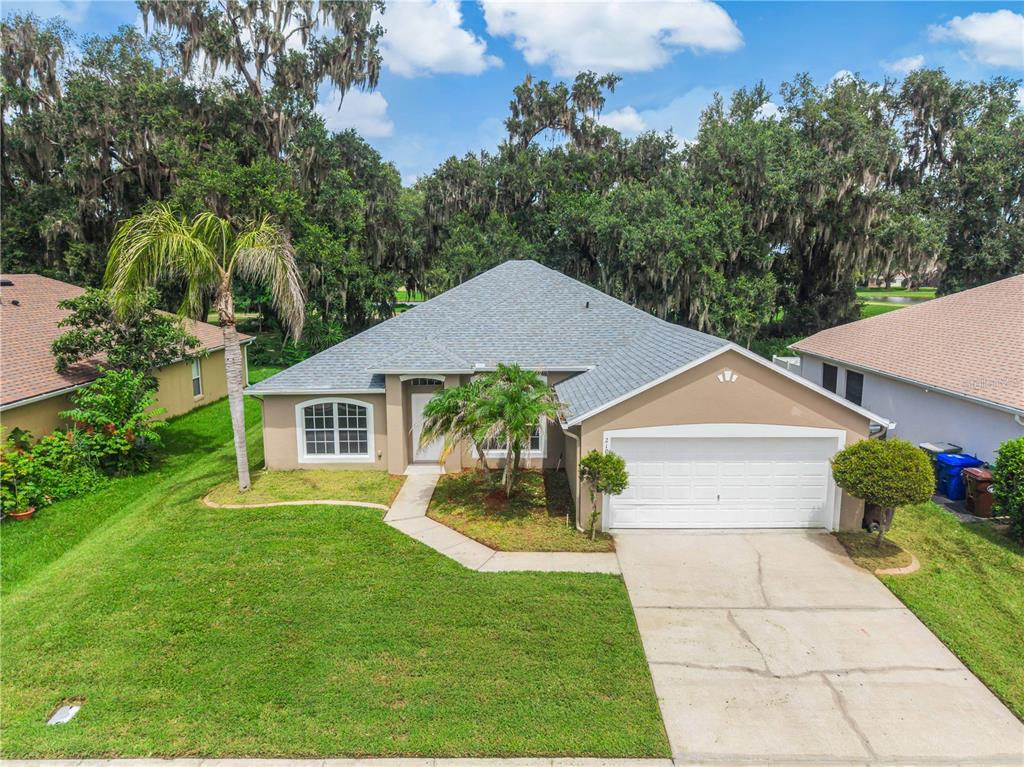 An exterior view of a single-story house with a gray roof, tan siding, and garage — 2106 THE OAKS BOULEVARD, KISSIMMEE, FL